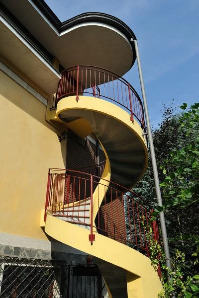 Scala elicoidale in calcestruzzo armato giallo con ringhiera in ferro rossa per villa a Piacenza