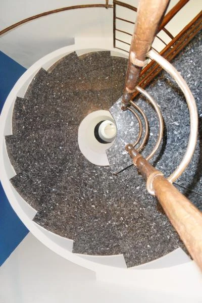 Vista dall'alto di una scala elicoidale prefabbricata in cemento armato con gradini in granito grigio e corrimano centrale in ottone